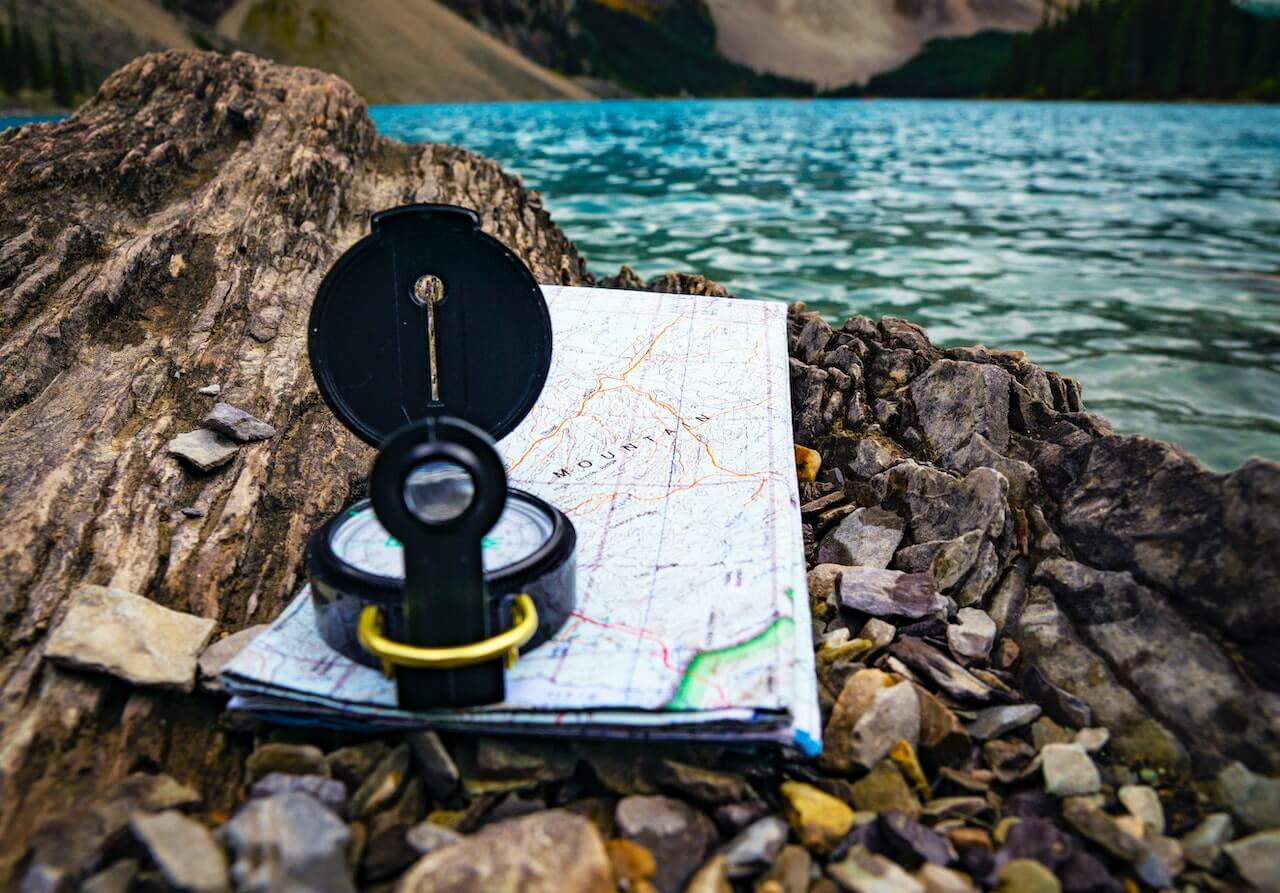 Ein Bild einer Karte und eines Kompasses auf einem Felsen in der Nähe eines ruhigen Sees, unverzichtbare Werkzeuge für Navigation und Erkundung.